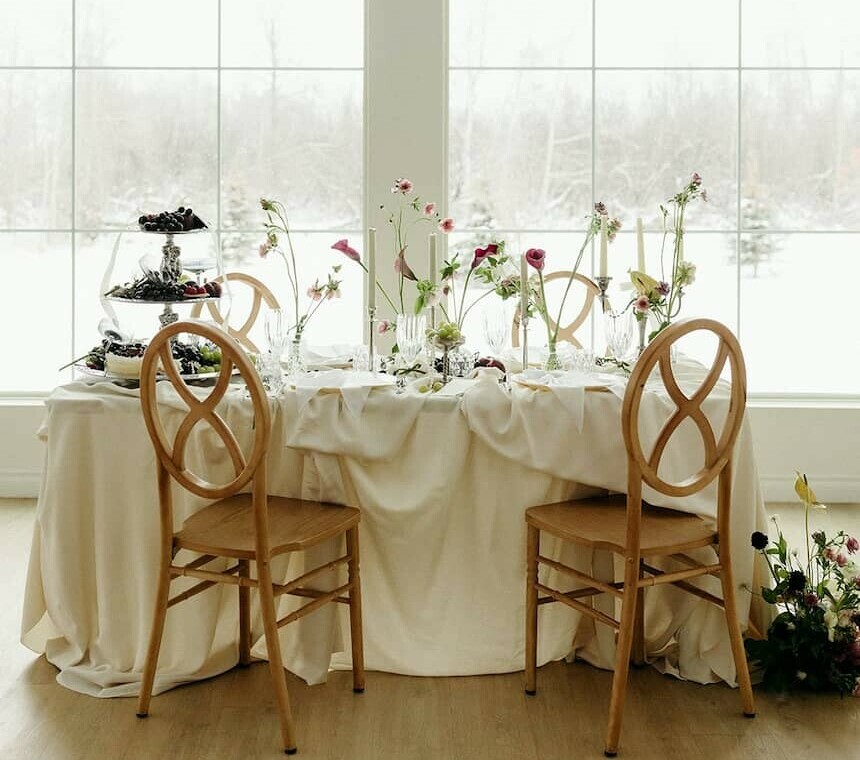 White linen rectangular table with floral centerpiece and Infinity wood chairs at a winter event